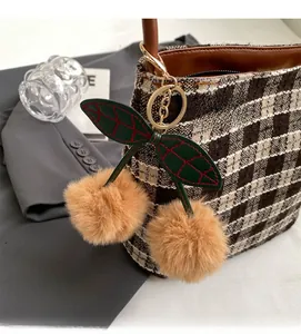 Détail du bijou de sac en fausse fourrure cerise avec feuilles sur un sac à carreaux