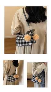 Detail of black and white plaid bag featuring plush pom-poms and leather strap