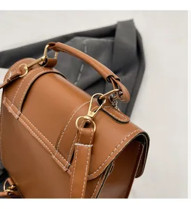 Detail view of brown leather backpack featuring gold metal hooks and white contrast stitching