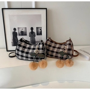 Close-up of checkered hobo bag with plush cherry charm on a minimalist display