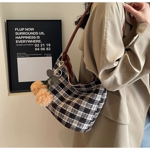 Détail d'un sac cabas en tweed à carreaux avec lanière en cuir et pompon doux