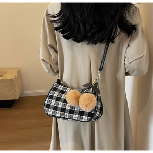 Detail of houndstooth shoulder bag featuring cherry-shaped pompom charm on model