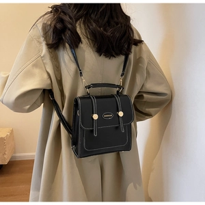 Close-up of black retro backpack with white stitching and gold buckles on khaki coat