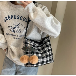 Détail d'un cabas en tweed noir et blanc avec pendentif cerise en peluche porté par un mannequin