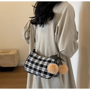 Detail of black and white checkered crossbody bag with cherry pom-pom charm on model