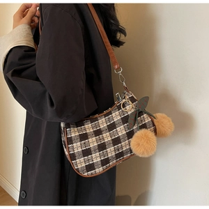 Brown plaid crossbody bag with plush charms and leather strap shown on shoulder