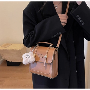 Detail of brown vintage PU leather bag with white stitching and panda plush charm