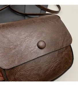 Close-up of vintage brown textured leather crossbody bag featuring a round buckle and stitching