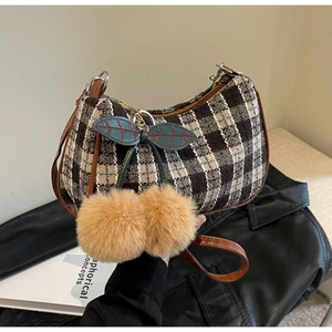 Detail view of plaid woven underarm bag with leather strap and plush cherry charm