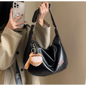 Détail du sac hobo en cuir noir avec étiquette FASHION et pendentif en peluche