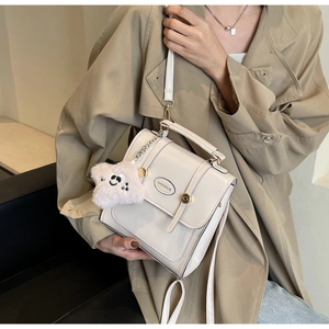 Close-up of beige glossy PU leather mini bag with gold hardware and plush bear charm