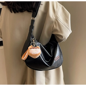 Détail du sac croissant plissé noir avec breloque peluche rose sur un trench-coat kaki