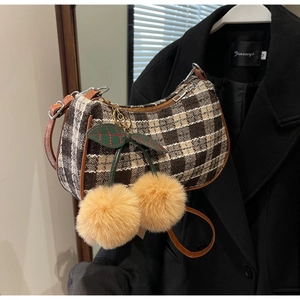Detail of checkered fabric shoulder bag with yellow plush cherry charm and brown leather strap