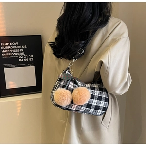 Detail of woven checkered shoulder bag with pink pom-poms and adjustable leather strap