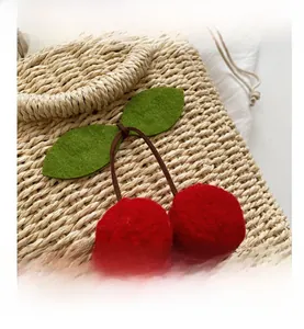 Close-up of a woven straw bag featuring handcrafted red cherry felt ornaments and green leaves