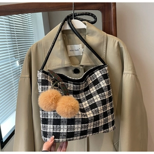 Détail du sac cabas en tweed à carreaux avec breloques en peluche sur un trench-coat