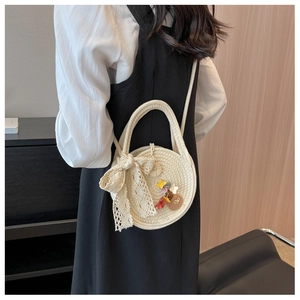 Détail du sac rond tressé beige avec nœud en dentelle et breloques de fleurs