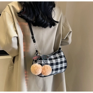 Detail of checkered shoulder bag with oversized cherry plush charm on beige coat