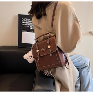Close-up of brown vintage leather backpack with white stitching and bear charm