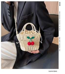 Detail of hand-woven straw bag with cherry charm and beige drawstring liner