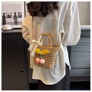 Detail of straw bucket bag featuring knit cherries, lace bow, and drawstring liner