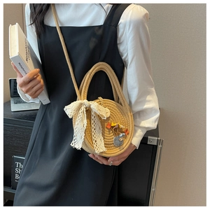 Détail d'un sac rond en paille avec nœud en dentelle et broderie porté par un mannequin
