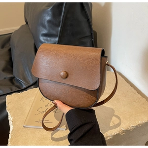 Detail view of the brown vintage saddle bag featuring a round button closure and leather texture