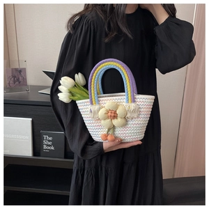 Detail of woven straw bag with rainbow handle and floral charm held by model