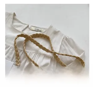 Detail of soft white cotton blouse featuring a natural woven straw crossbody strap