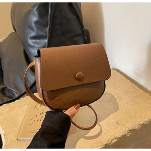 Detailed view of brown vintage saddle bag featuring litchi texture and round buckle closure