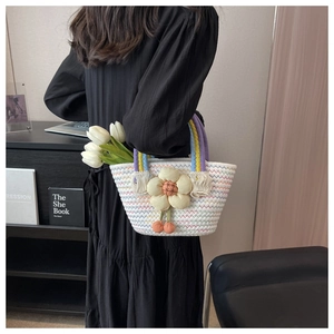 Detail of woven tote bag with yellow floral embellishment and orange pom-poms charms