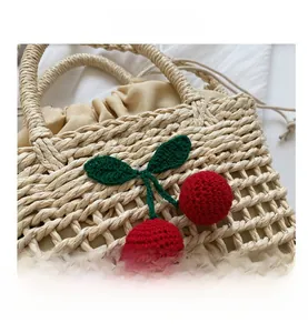 Detail of hand-woven straw bag featuring red crochet cherry charms and beige drawstring liner