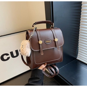 Close-up of vintage brown leather backpack with contrast stitching and plush ball charm