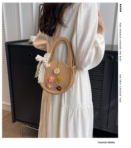 Detail einer runden Strohtasche mit bunten Blumen-Applikationen und Spitzenschleife