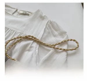 Detail of hand-woven straw bag shoulder strap paired with a white cotton linen top