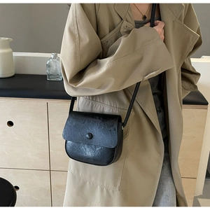 Detail of a black pleated crossbody bag styled with a khaki trench coat in a minimal interior
