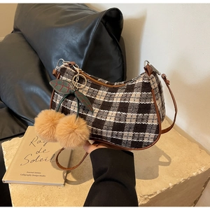 Detail of tweed crescent underarm bag with a plush cherry charm on a stone base