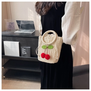 Detail of hand-woven straw bag with red cherry accents and a drawstring inner pouch