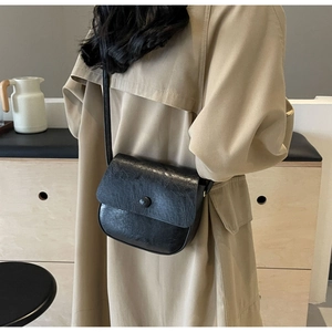 Detail of a black pleated crossbody bag featuring a half-round flap and single button closure