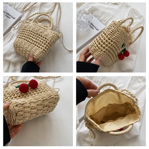 Detail of hand-woven straw bucket bag with red cherry charm and drawstring lining