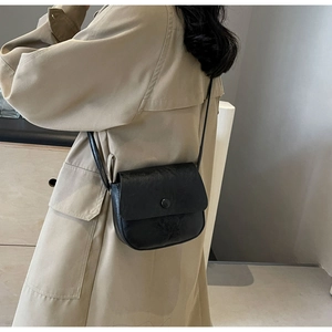 Close-up of minimalist black leather crossbody bag with rounded base and decorative button