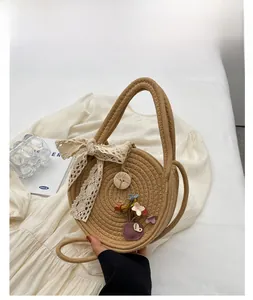 Détail d'un sac à main rond en paille avec nœud en dentelle et bouton en bois sur texture
