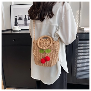 Detail of a beige woven straw bucket bag with red cherry motifs and drawstring closure