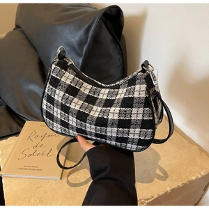 Close-up of black and white checkered tweed shoulder bag with leather piping on stone surface