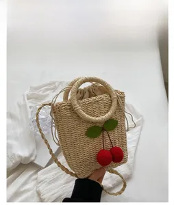 Detail of white woven straw bucket bag with red cherry accents and drawstring closure