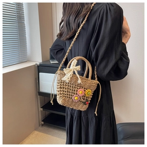 Detail of hand-woven straw bucket bag with floral accents and lace bow on a black dress
