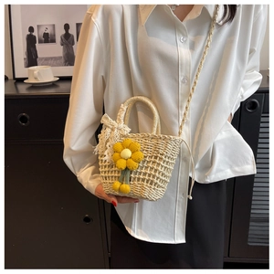 Detail of beige straw bucket bag with yellow knit flowers and white lace bow decoration
