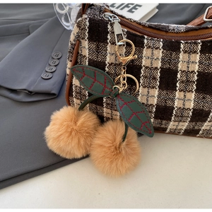 Detailed close-up of plush cherry bag charm with green leaves and red stitching details