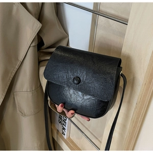 Close-up of black retro saddle bag with oil wax texture paired with khaki trench coat