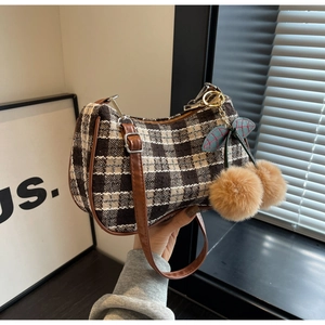 Detail of tweed checkered underarm bag with leather strap and plush cherry pendant charm